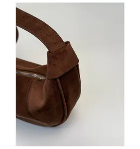 Detailed close-up of reinforced handle stitching and metal zipper on brown suede bag