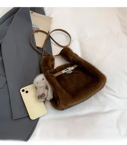 Detail of plush brown bucket bag with leather strap and mini rabbit charm on white bed