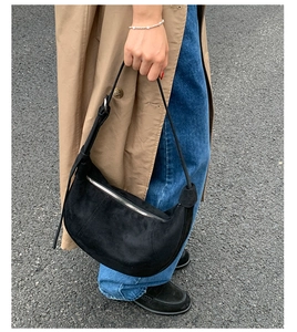 Close-up of a black suede crescent shoulder bag with silver zipper and knot detail