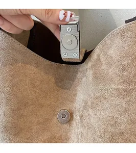 Macro shot of circular magnetic snap closure and fine stitching on suede leather handbag