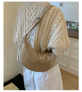 Close-up of beige suede crescent bag worn by model in a cozy kitchen setting