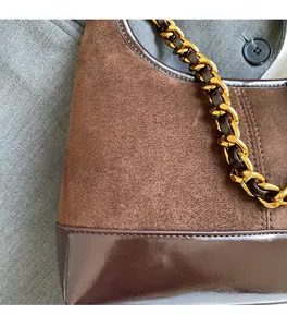 Detailed close-up of brown suede and glossy leather patchwork with a chunky gold chain strap
