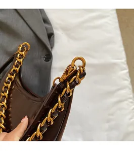 Detail of glossy brown leather handbag with robust gold chain strap and metal clasp