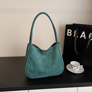 Close-up of a dark green suede hobo bag with matching shoulder strap on a display table