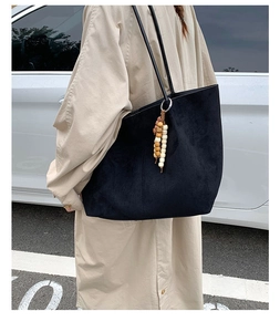 Black suede tote bag detail showing texture and wooden bead pendant for autumn commuting.