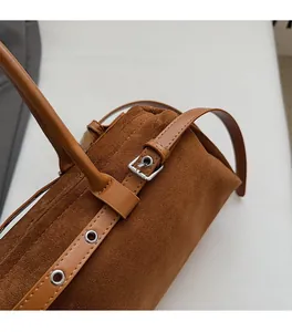 Close-up of brown suede shoulder bag showing silver metal buckles and leather stitching
