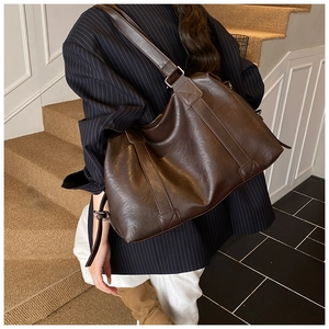 Detail view of large dark brown leather tote bag with wide shoulder straps and retro texture