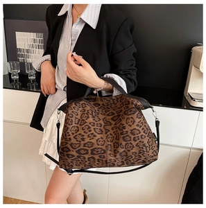 Detail of the leopard print tote bag featuring black leather straps and a woven side tag