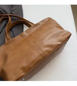 Close-up of brown tote bag with leather texture, decorative stitching and metal studs