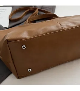 Detail view of the brown leather tote base featuring silver metal feet and neat stitching