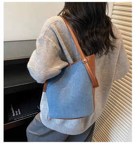 Detail of blue denim bucket bag with brown leather trim and slim shoulder strap