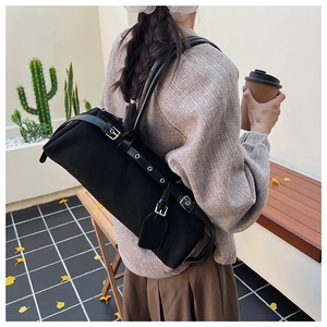 Close-up of black canvas cylinder baguette bag with silver buckle shoulder strap detail
