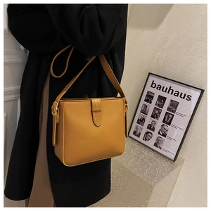 Detail der senfgelben quadratischen Ledertasche, getragen über einem schwarzen Wollmantel