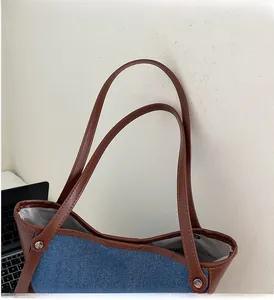 Detail of blue denim and brown faux leather tote bag showing handle rivet reinforcement