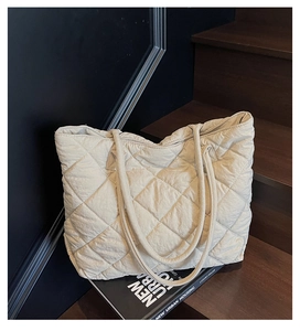 Detailed view of beige quilted nylon tote bag with rhombus pattern on wooden stairs