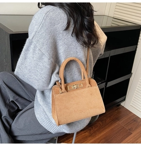 Detail of vintage camel suede handbag with gold hardware shown on a model