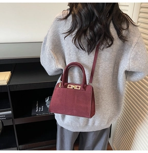 Detail view of burgundy suede crossbody bag with gold hardware on a grey sweater