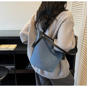 Detail of blue denim bucket bag with black leather trim worn on model's shoulder
