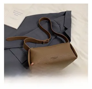Close-up of litchi grain texture on brown crossbody pillow bag with wide shoulder strap