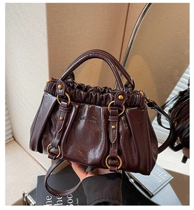 Detail of dark brown glossy leather pleated bag with gold buckle and stylish shoulder strap