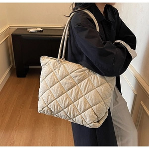 Grand sac fourre-tout matelassé blanc cassé porté à l'épaule dans un décor intérieur