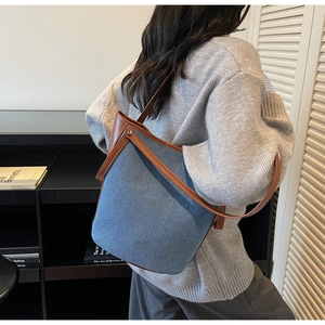 Close-up of bucket bag showing blue denim and brown leather patchwork with metal rivets