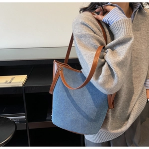 Detail of blue denim bucket bag with brown leather trim and slim shoulder straps