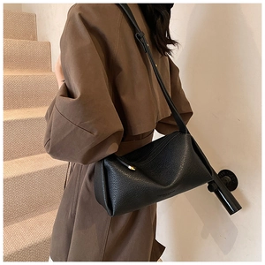Detail of a black litchi grain leather crossbody bag worn over the shoulder by a model