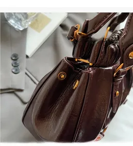 Detail of glossy pleated leather and gold hardware on dark brown shoulder bag