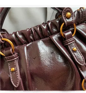 Detailed view of dark burgundy pleated leather with gold hardware and embossed logo