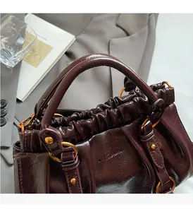 Detail of dark burgundy pleated leather handbag featuring retro gold metal hardware