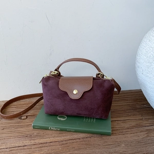 Detailed view of burgundy suede handbag with brown leather flap and gold hardware accents