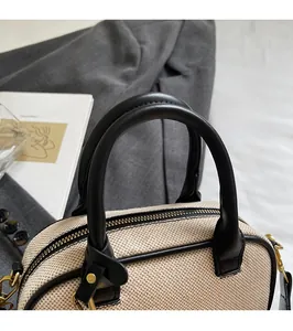 Detail van ronde handgrepen en gouden hardware op een beige geweven Boston handtas