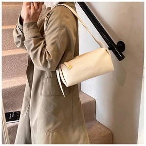 Close-up of beige textured leather cylinder bag featuring elegant gold hardware details