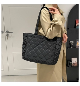 Detail of black quilted tote bag with diamond pattern worn over a beige trench coat