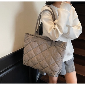 Grey quilted tote bag with diamond stitching shown on shoulder in a minimalist indoor setting
