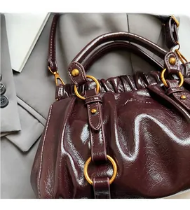Close-up of wine red glossy wrinkled leather handbag with gold metal rings and studs