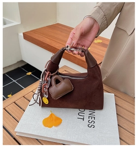 Nahaufnahme der braunen Wildledertasche mit Metallschnalle und Herzanhänger auf Holztisch