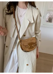 Detail of brown saddle bag with gold buckles and mixed textures on a trench coat