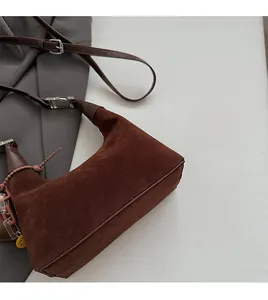 Detail view of dark brown suede crescent bag with silver buckles and a yellow smiley charm