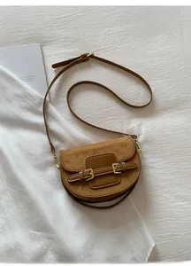Detailed top view of a dark brown saddle bag with mixed textures on a white fabric background
