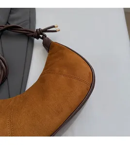Detail of brown suede crescent bag featuring a knotted shoulder strap and gold hardware