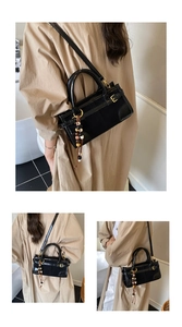 Detail of black glossy baguette bag featuring gold hardware and colorful beaded tassel