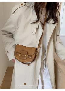 Brown retro saddle bag with gold buckles worn over a beige trench coat for a minimalist look