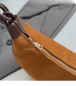 Detail of caramel suede crescent bag with smooth gold-toned zipper and fine stitching