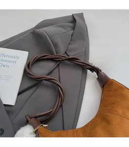 Detail of a brown suede half-moon bag with woven leather strap and white pompom charm