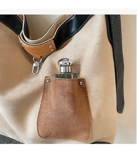 Close-up of beige suede tote with brown leather pocket, metal rivets and contrast stitching