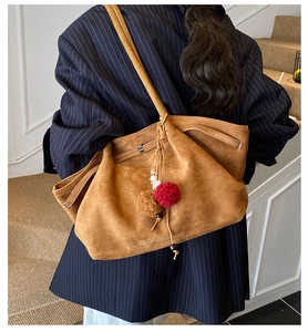 Détail d'un grand sac cabas en daim marron avec des breloques à pompons et texture mate