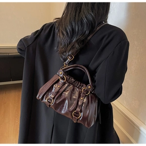 Detail of dark brown glossy leather handbag with gold hardware and pleated texture