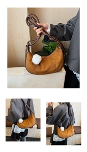 Detail view of brown crescent shoulder bag with knotted strap and white pompom accessory